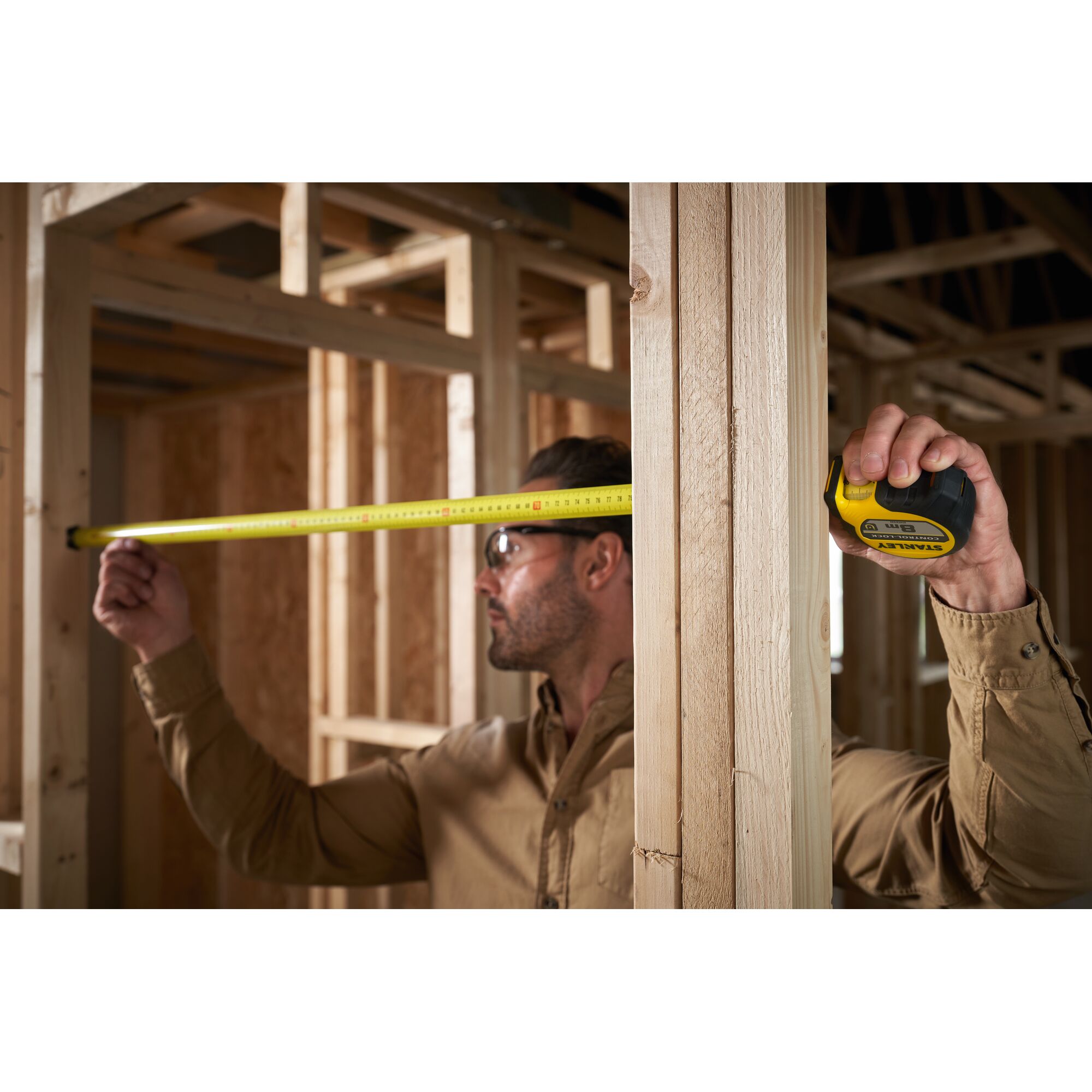 Person using STANLEY STHT37232-0 tape measure to measure wooden frame during construction.